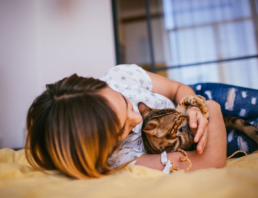 A woman lying down and hugging her Bengal cat.