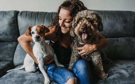 A joyful woman spending time with two emotional support animals indoors on a couch, wondering, “Can a landlord limit the number of emotional support animals?”