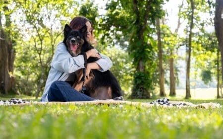 A happy woman hugging her emotional support animal while enjoying a sunny day at the park.