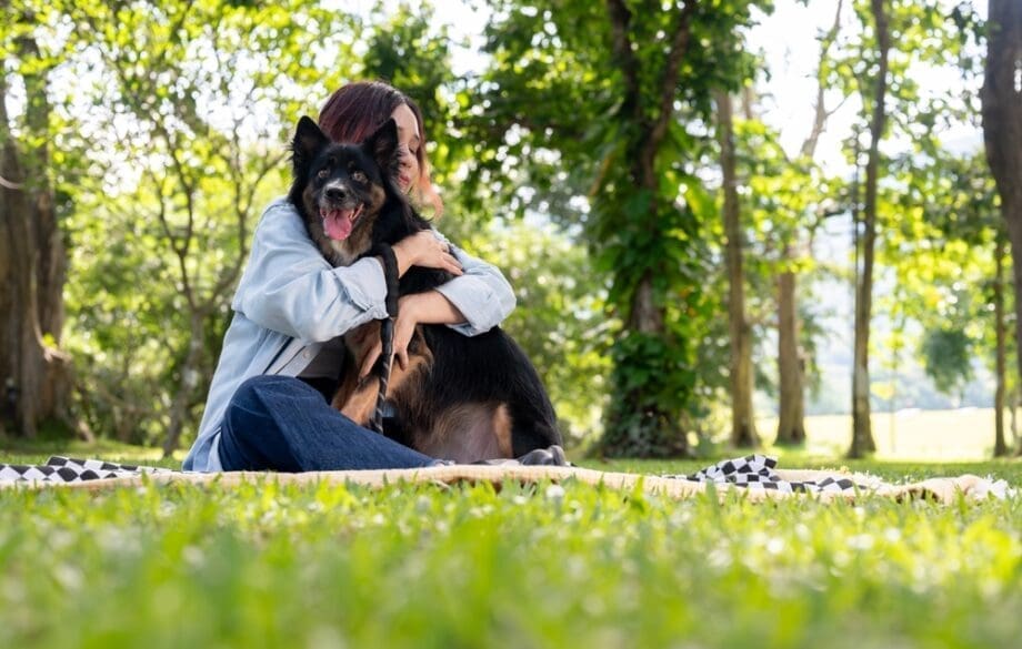 A happy woman hugging her emotional support animal while enjoying a sunny day at the park.