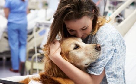 A young female patient lovingly holds a pet therapy dog in hospital, happy to receive the benefits of pet therapy.