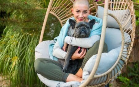 A young girl hugging bulldog in swing chair outside.